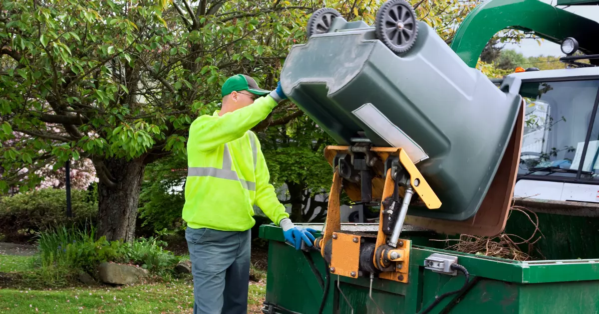 Worker using a truck lift for yard waste removal in a residential area