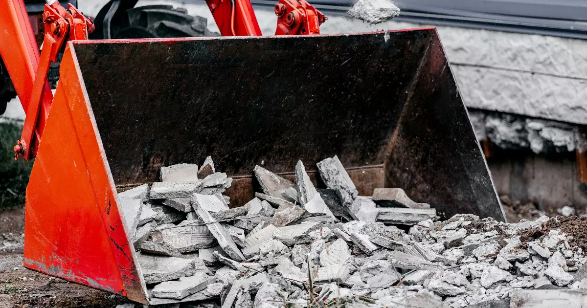 Excavator bucket loaded with broken concrete pieces during construction debris removal